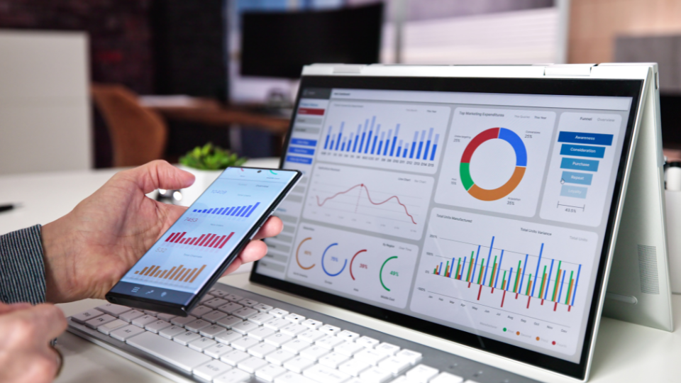 A person compares marketing analytics dashboards on a smartphone and a tablet at their desk.
