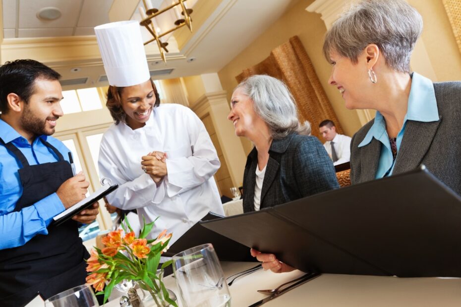 Chef and waiter interacting with smiling customers in a restaurant
