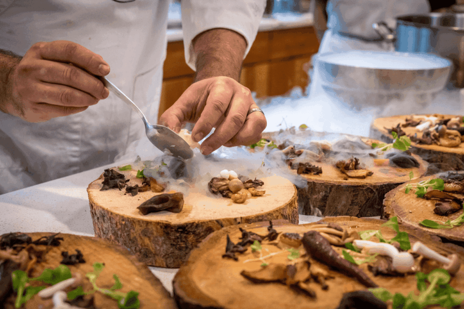 Chef plating gourmet food with a smoke effect on wooden boards