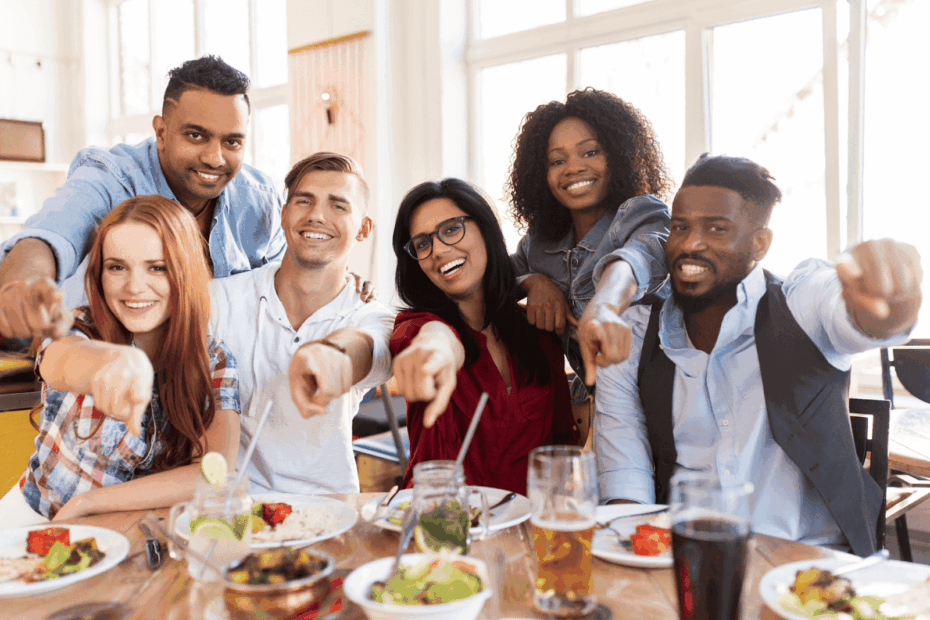 Group of friends at a restaurant table, pointing playfully at the camera
