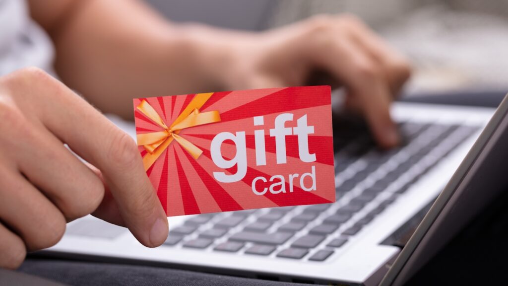 Hand holding a red gift card near a laptop
