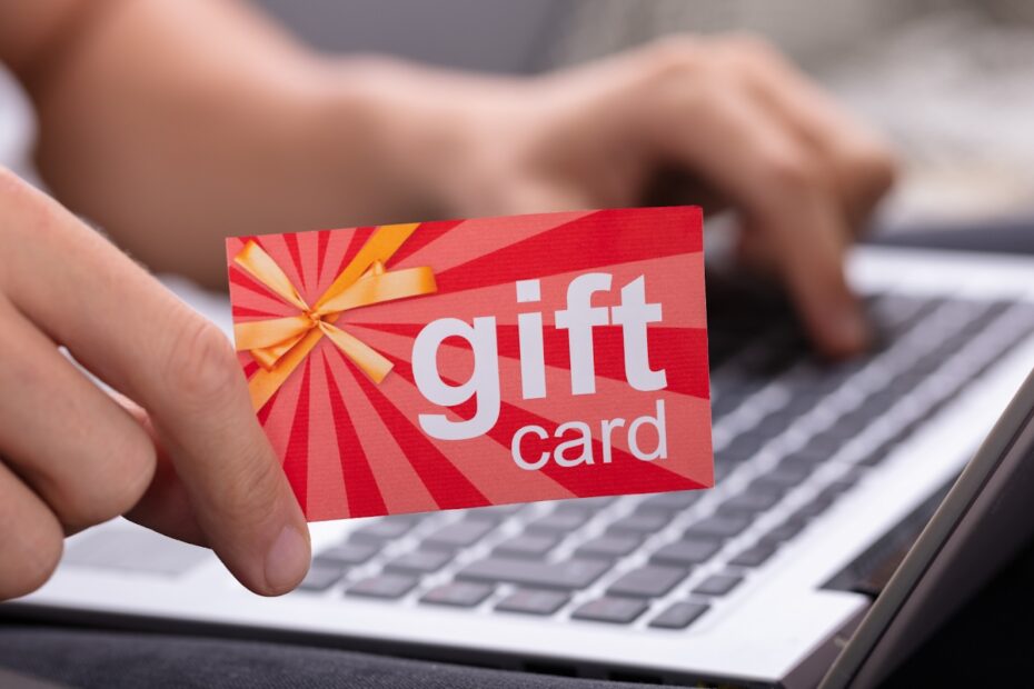 Hand holding a red gift card near a laptop