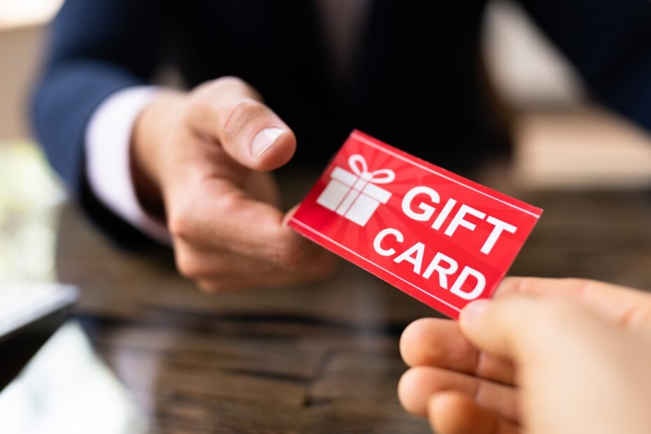 Person handing a red gift card across a wooden table