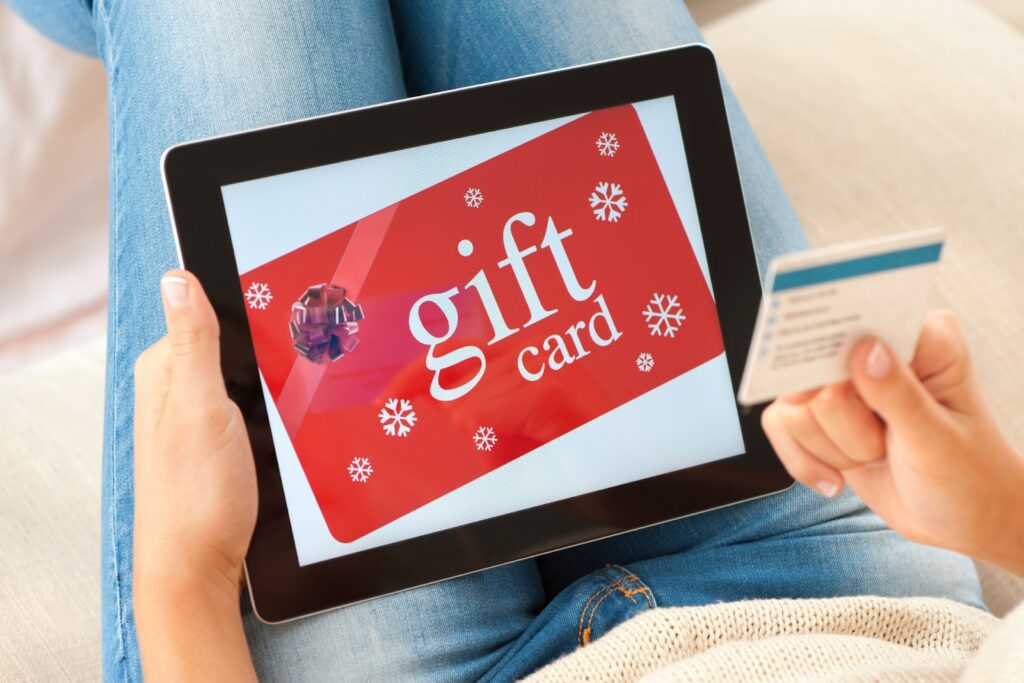 Person holding a tablet displaying a red digital gift card with snowflake decorations while holding a credit card