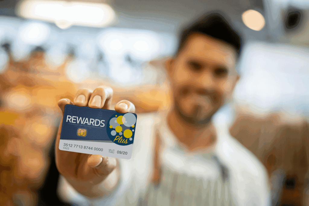 Smiling man in a store holding a blue rewards card with a yellow bubble design and the word “Plus” written on it