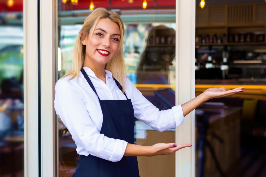 Smiling restaurant staff member standing at the entrance, gesturing to welcome guests