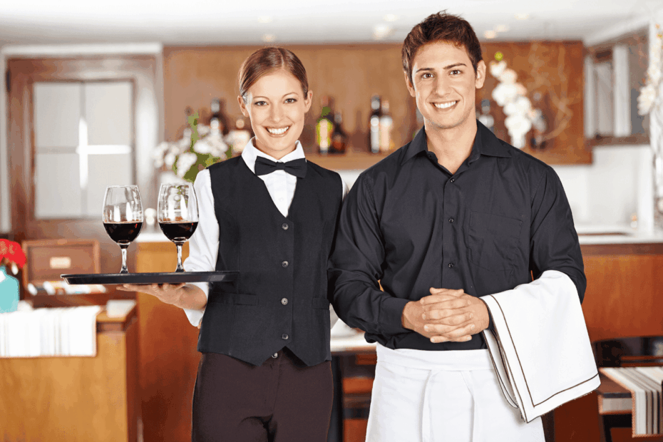 Two waiters smiling, one holding a tray with glasses of red wine.