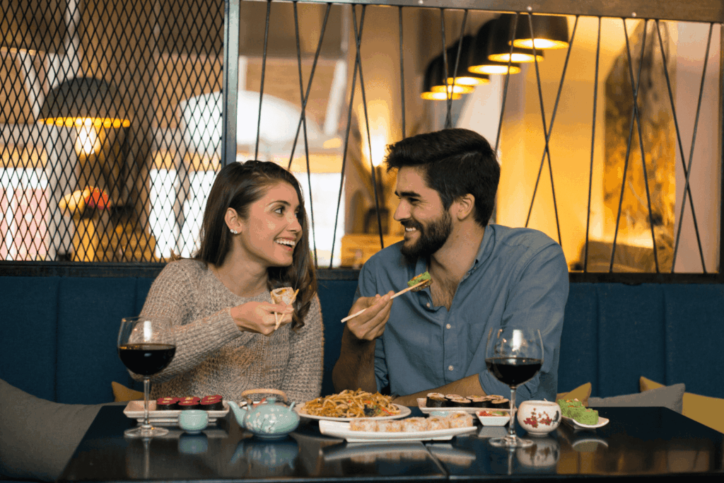 A couple shares a joyful moment over sushi and wine in a cozy, ambient restaurant setting.