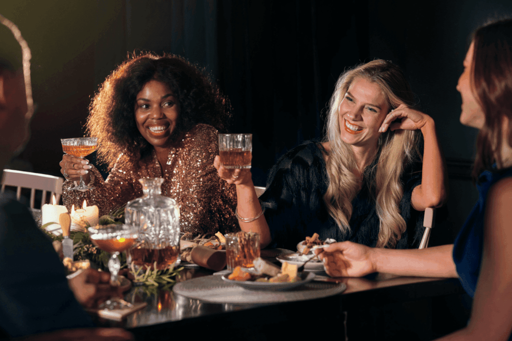 A group of elegantly dressed friends enjoy drinks together at a candlelit dinner party.