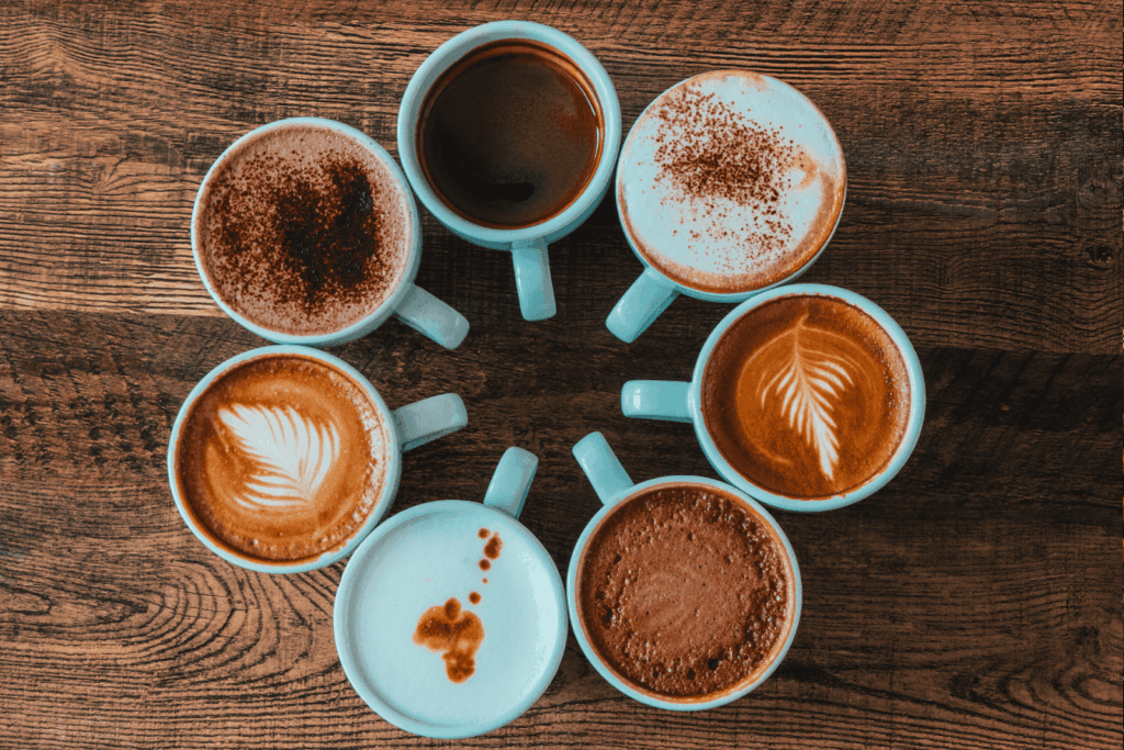 Eight coffee cups arranged in a circular pattern on a wooden surface, each featuring different coffee styles and latte art.