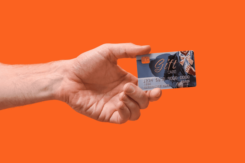 Hand holding a gift card with a ribbon design against an orange background.