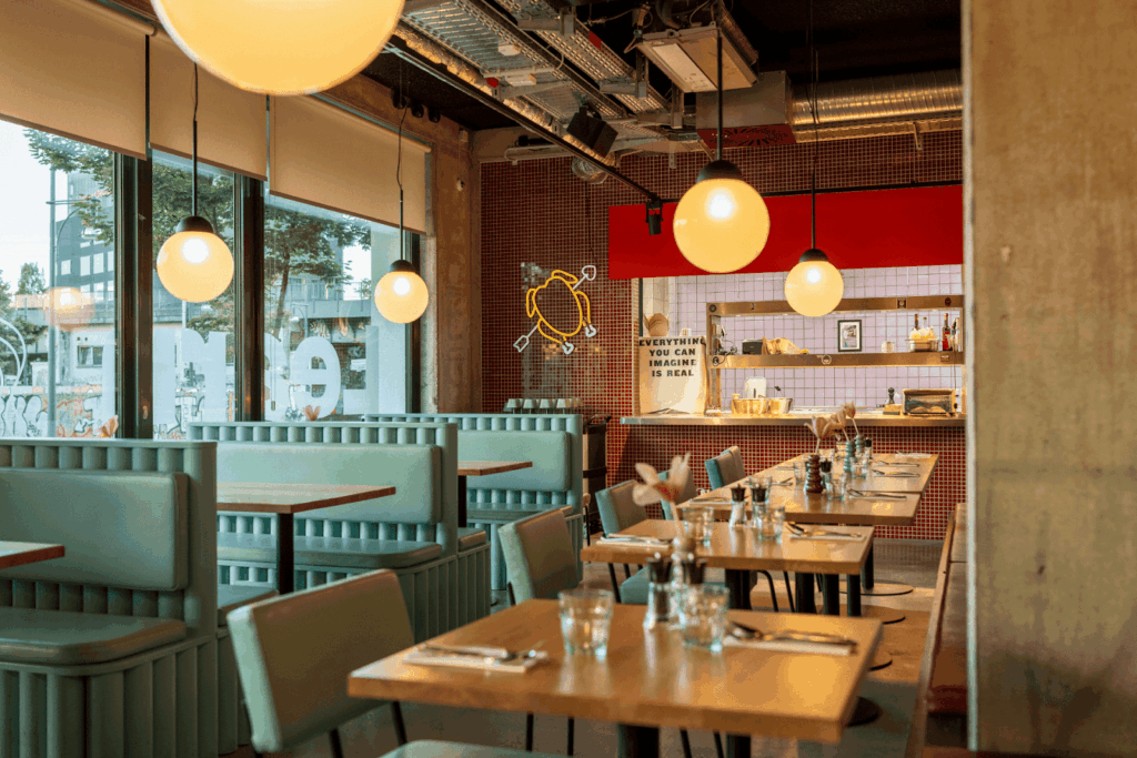 Modern restaurant interior with teal booths, wooden tables, and hanging globe lights.