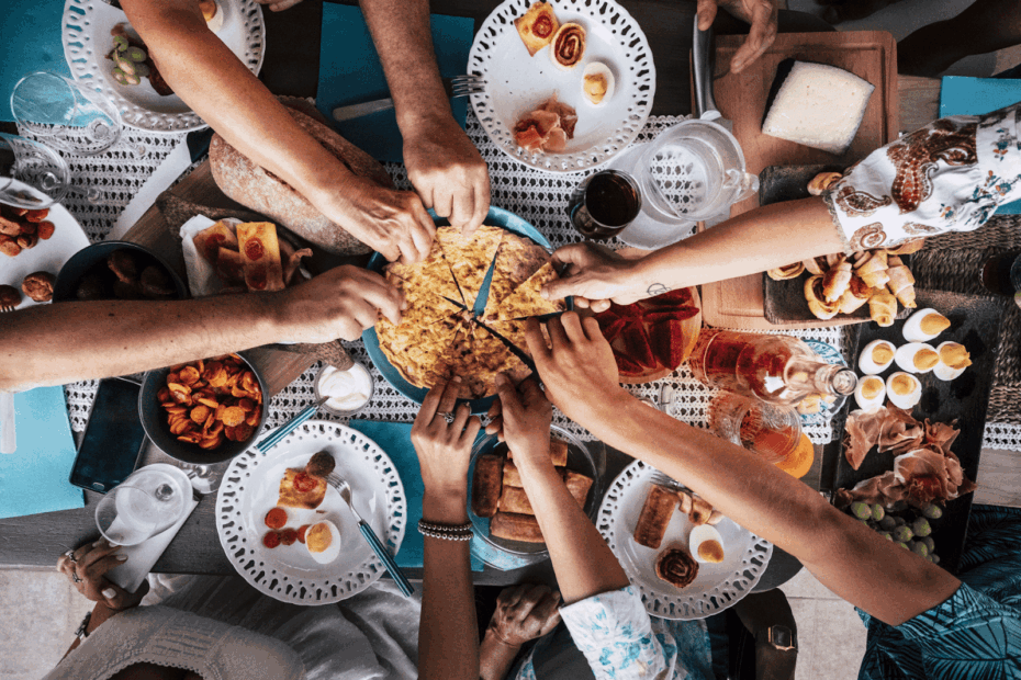 Several hands reach to grab slices of a large shared dish during a vibrant group meal.