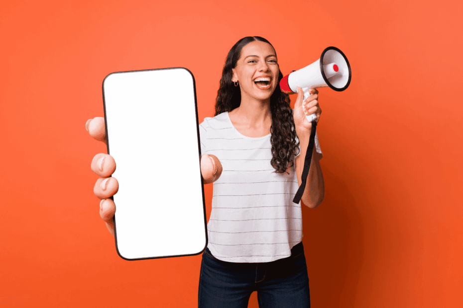 Smiling woman on an orange background holding a megaphone and a smartphone with a blank screen