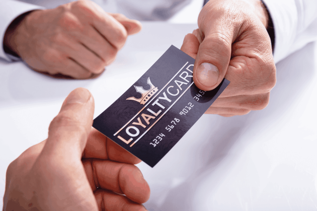 Two hands exchanging a black loyalty card with a crown symbol and silver text.