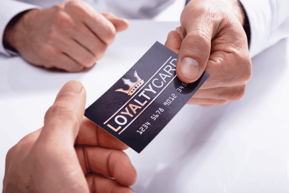 Two hands exchanging a black loyalty card with a crown symbol and silver text.