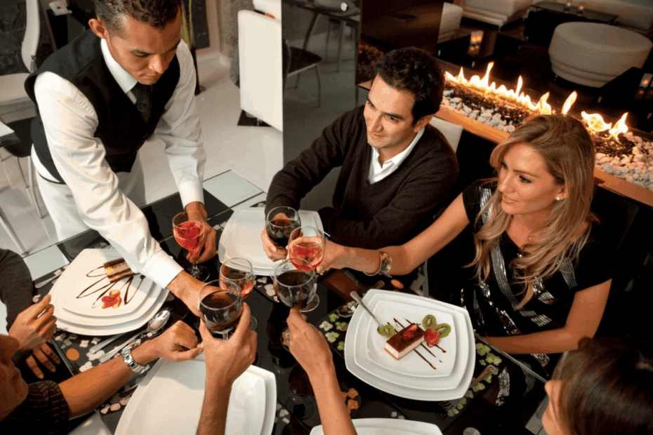 Waiter serving drinks to a group of people raising glasses for a toast in a restaurant.