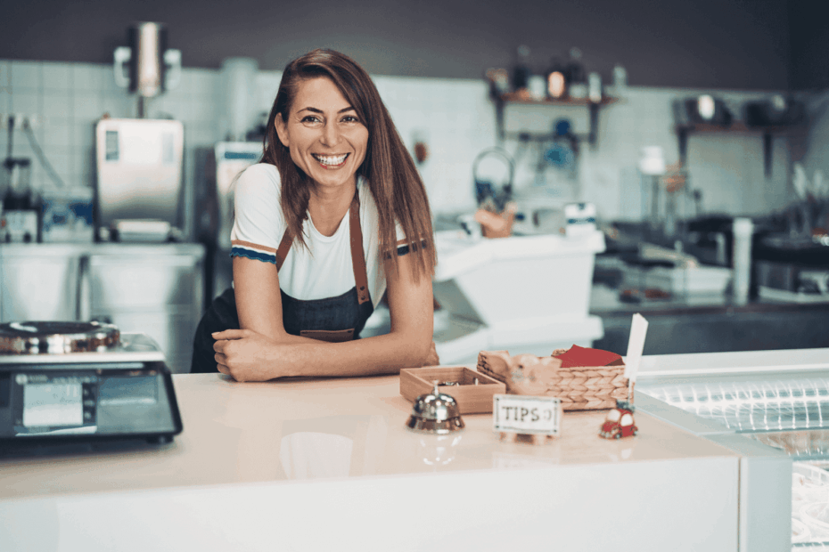 Woman in an apron smiling behind the counter of a modern café