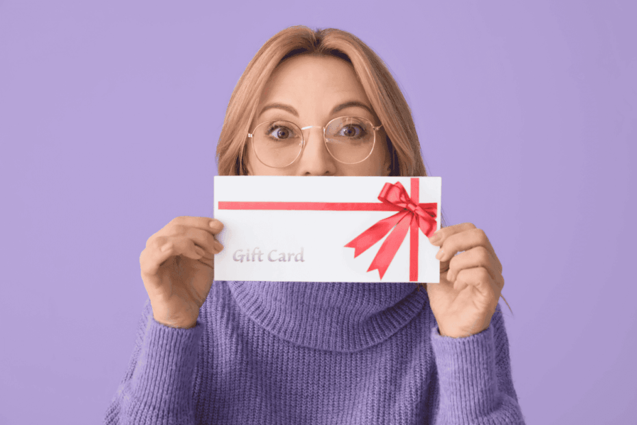 Woman in glasses holding a white gift card envelope with a red ribbon