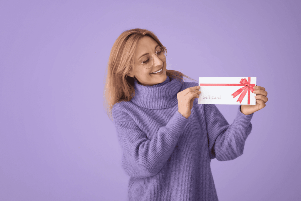 Woman in purple sweater holding a gift card with a red ribbon on a purple background.