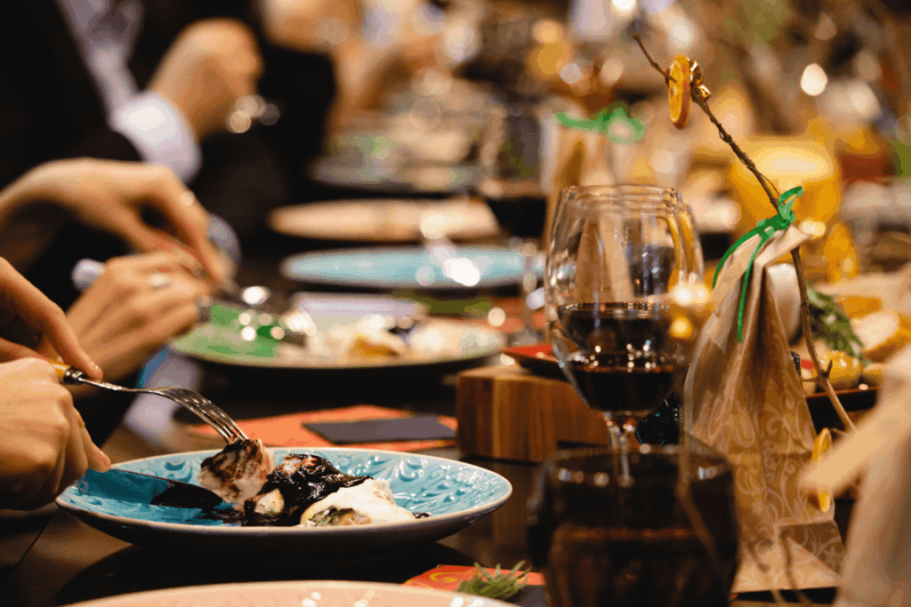 Close-up of a festive dinner table with plates, wine glasses, and people eating.