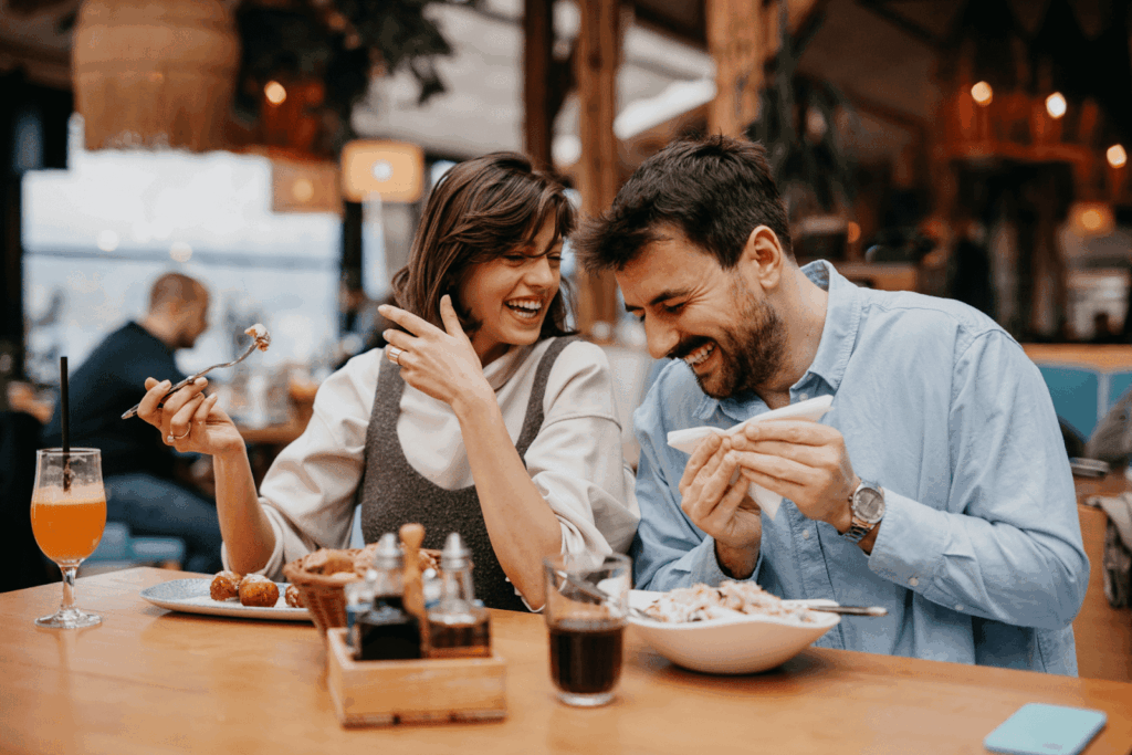 A couple laughing together while eating at a restaurant.