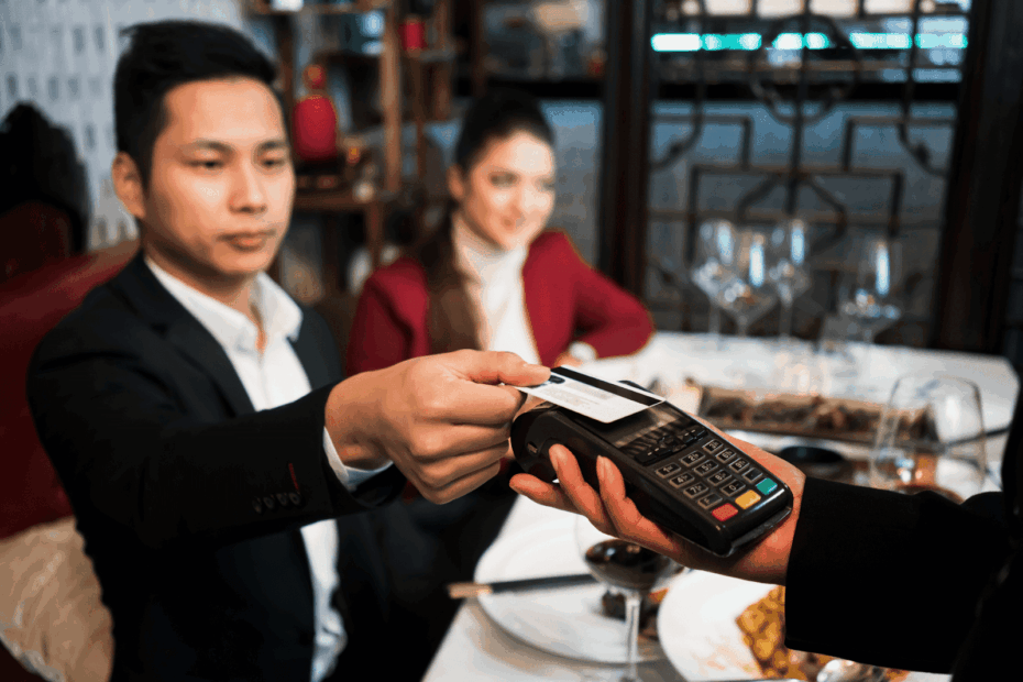 A diner paying with a credit card using a handheld card reader at a restaurant table.