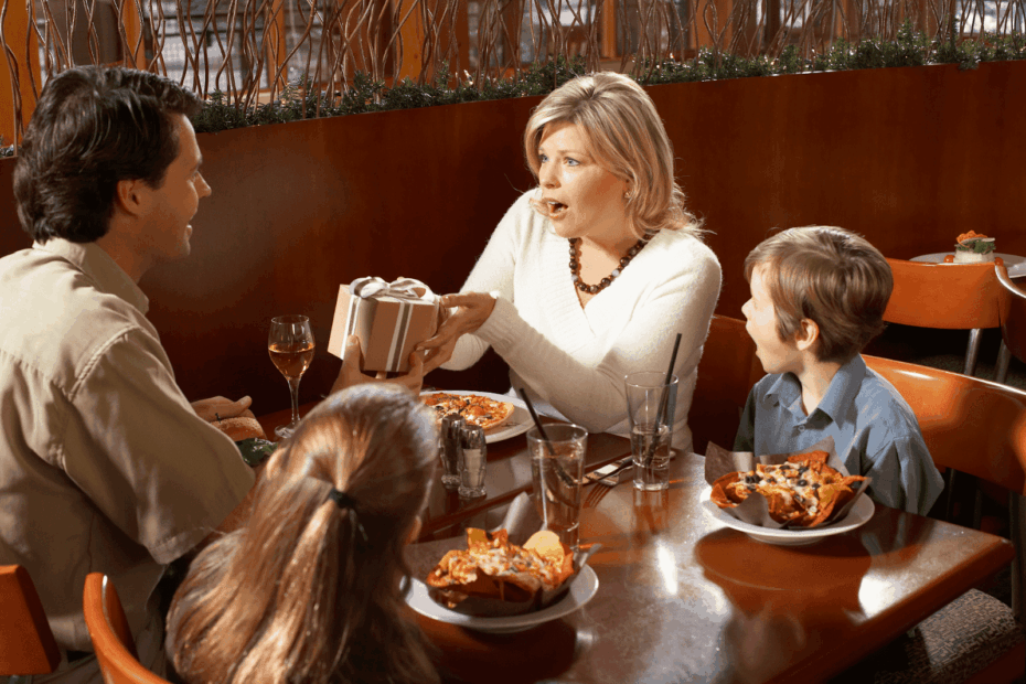 A family dining at a restaurant while a woman receives a wrapped gift.