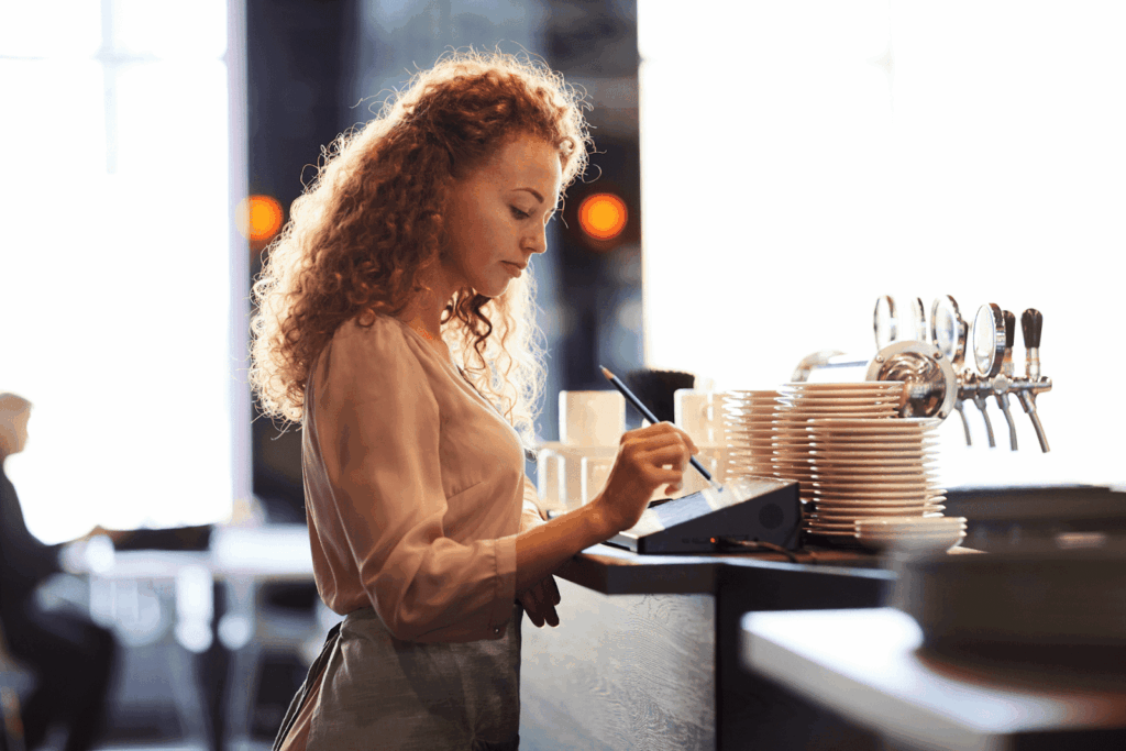 A server using a touchscreen register behind the counter in a brightly lit café.