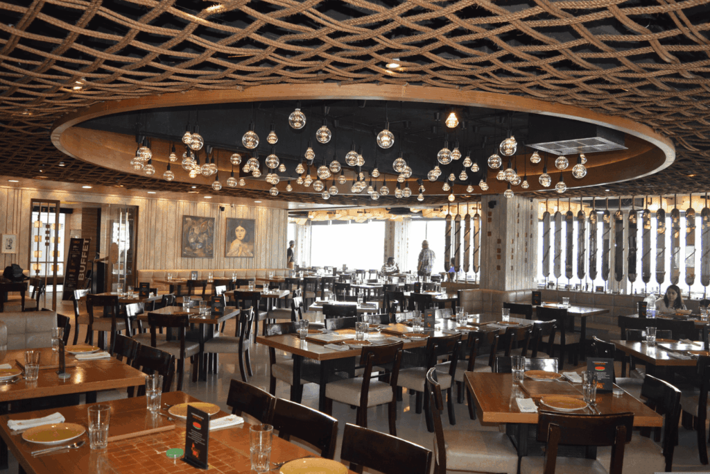 A spacious restaurant dining room with wooden tables, hanging glass lights, and decorative rope ceiling details.