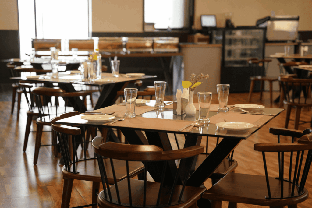 An empty restaurant dining area with wooden tables set with glasses and plates.