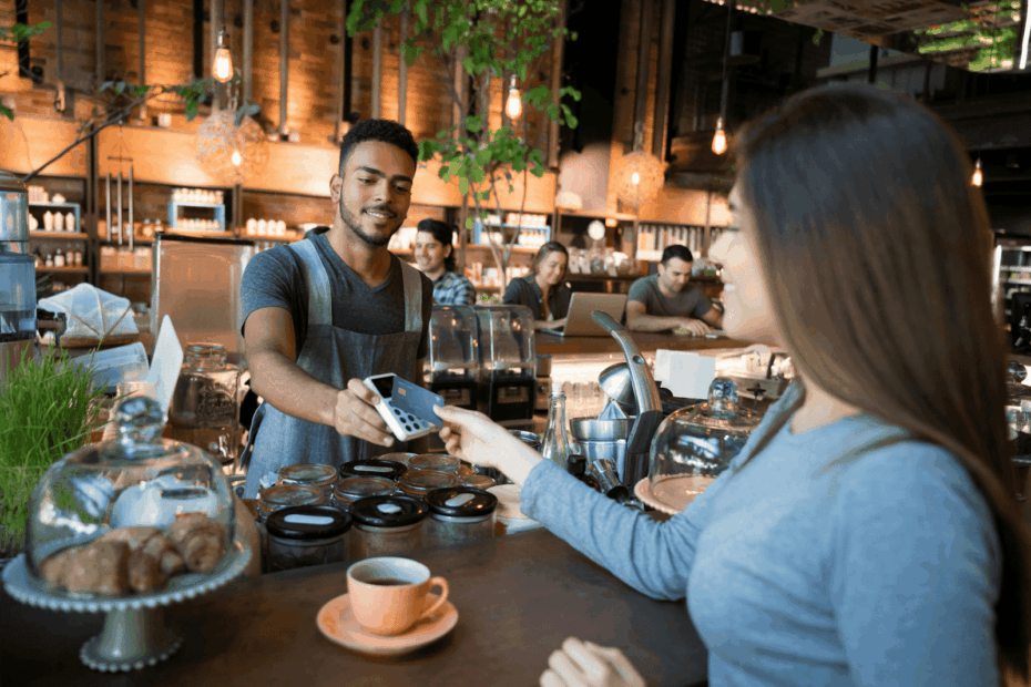 Barista handing a payment terminal to a customer at a cozy café counter.