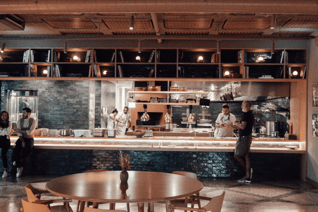 Chefs working in an open restaurant kitchen with people standing at the counter.