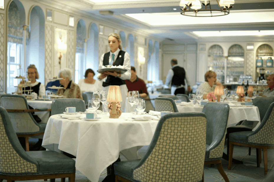Elegant dining room with guests seated as a server carries a tray of food.