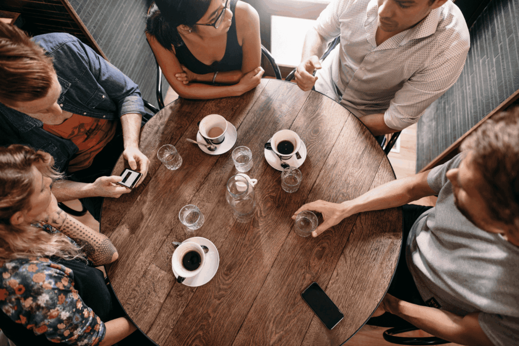 Five people sitting around a café table with coffee cups, talking.