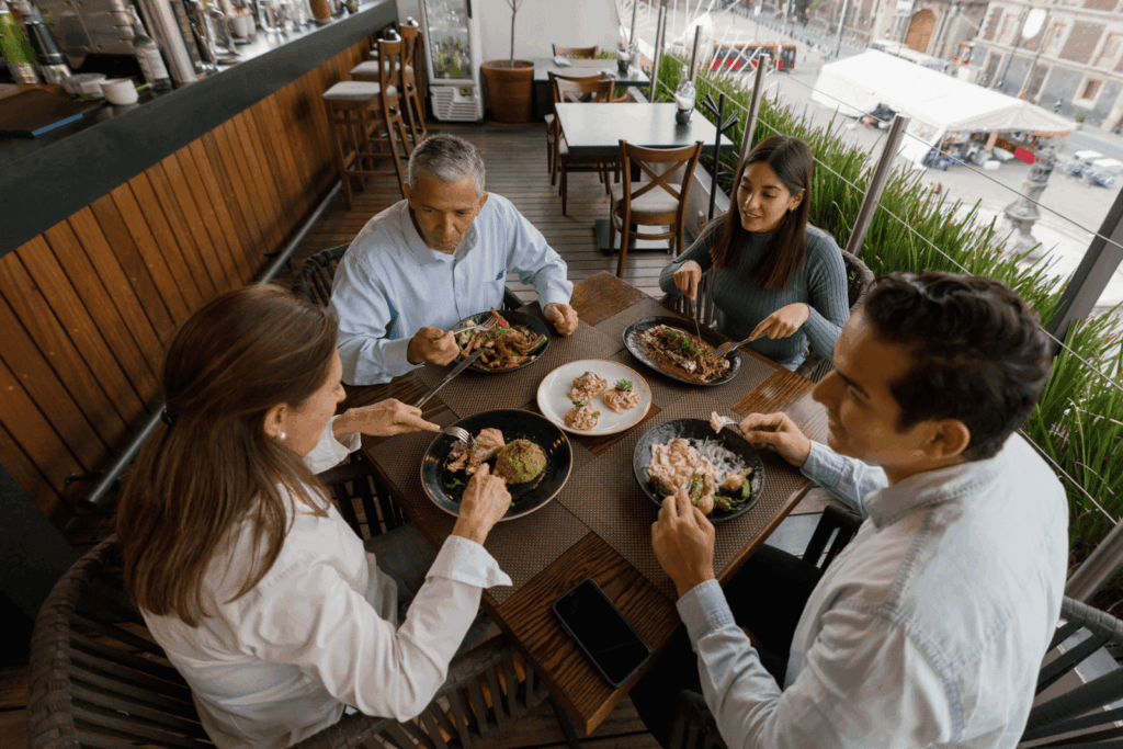 Four people dining together at an outdoor restaurant table with assorted dishes.