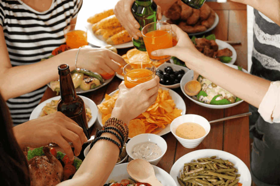 Friends clinking drinks over a table filled with shared food dishes.