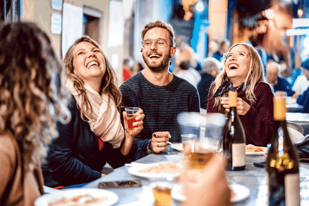 Friends gathered at an outdoor table, laughing and drinking together.