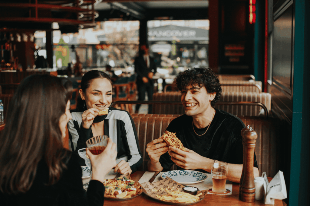 Friends laughing and eating together at a restaurant table.