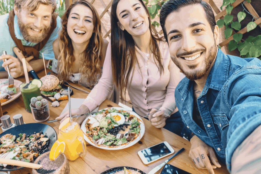 Friends taking a selfie while enjoying a meal together at an outdoor café.