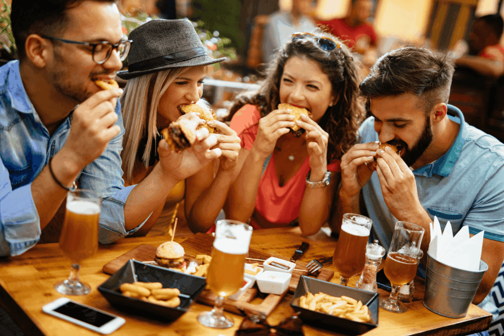 Group of friends eating burgers and fries together at an outdoor table.