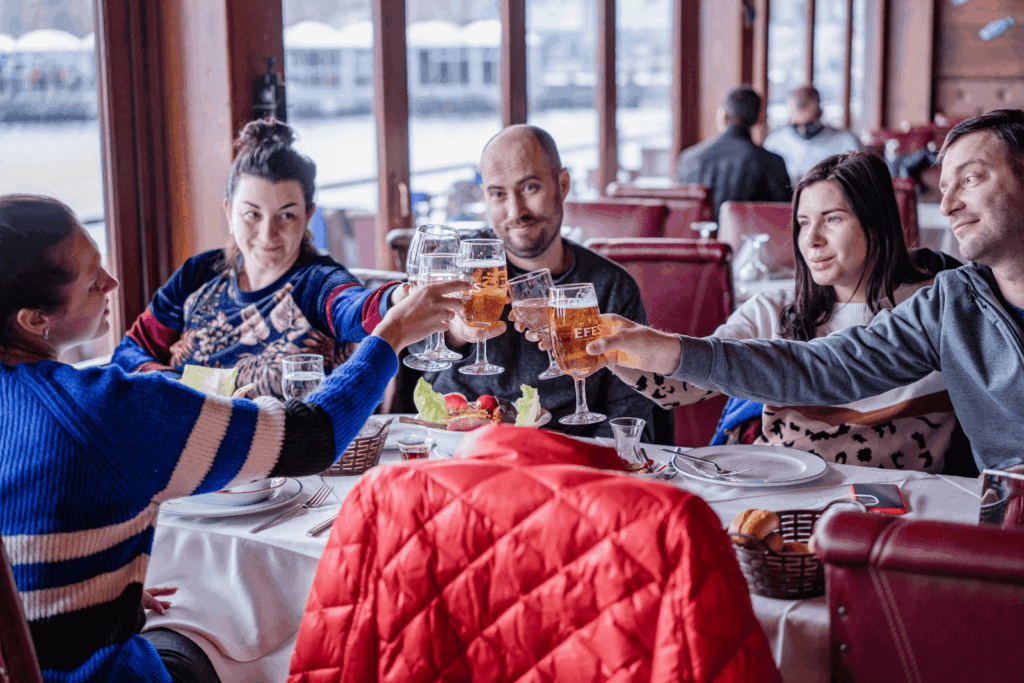 Group of friends raising beer glasses for a toast at a restaurant table.