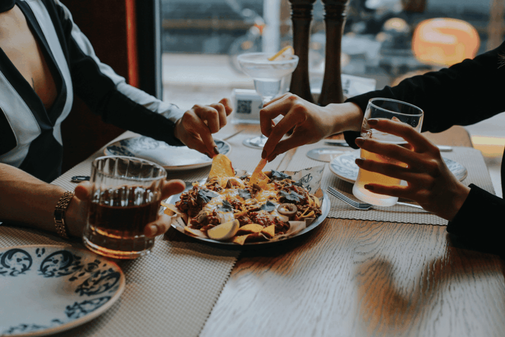 Hands reaching for nachos while holding drinks at a restaurant table.