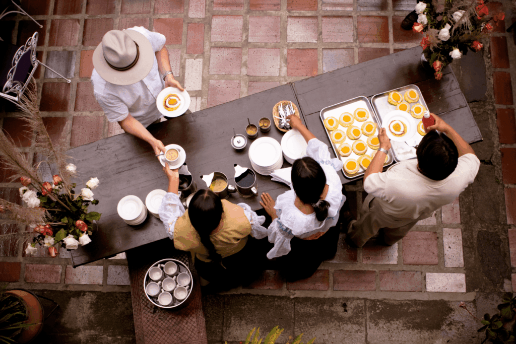 Overhead view of staff serving desserts and coffee to a customer at a long outdoor table.