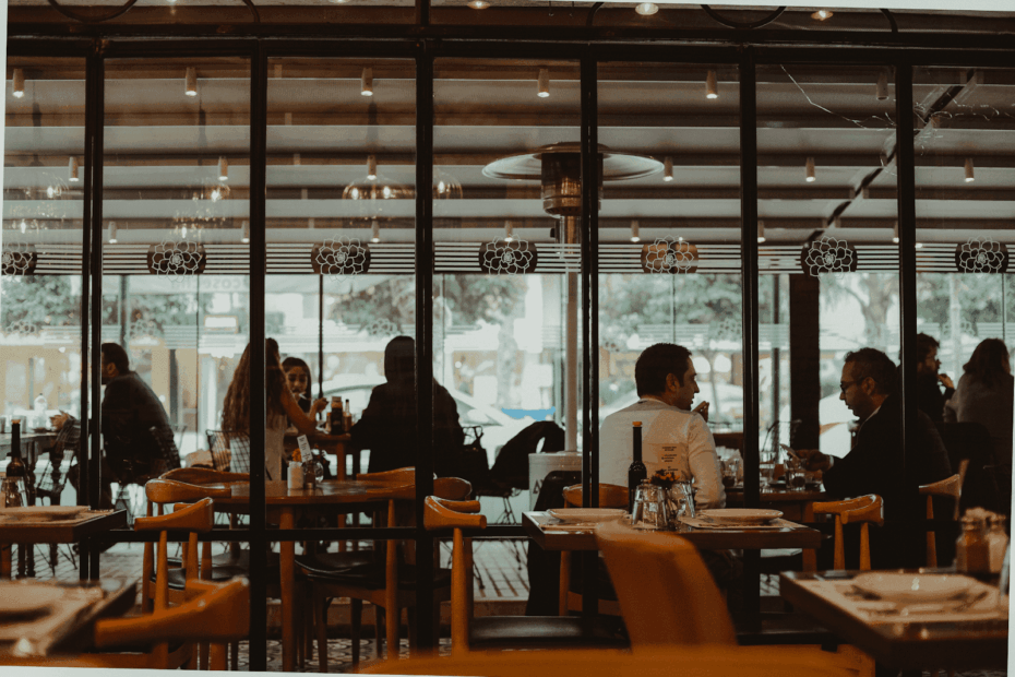 People dining and talking inside a restaurant seen through large glass windows.