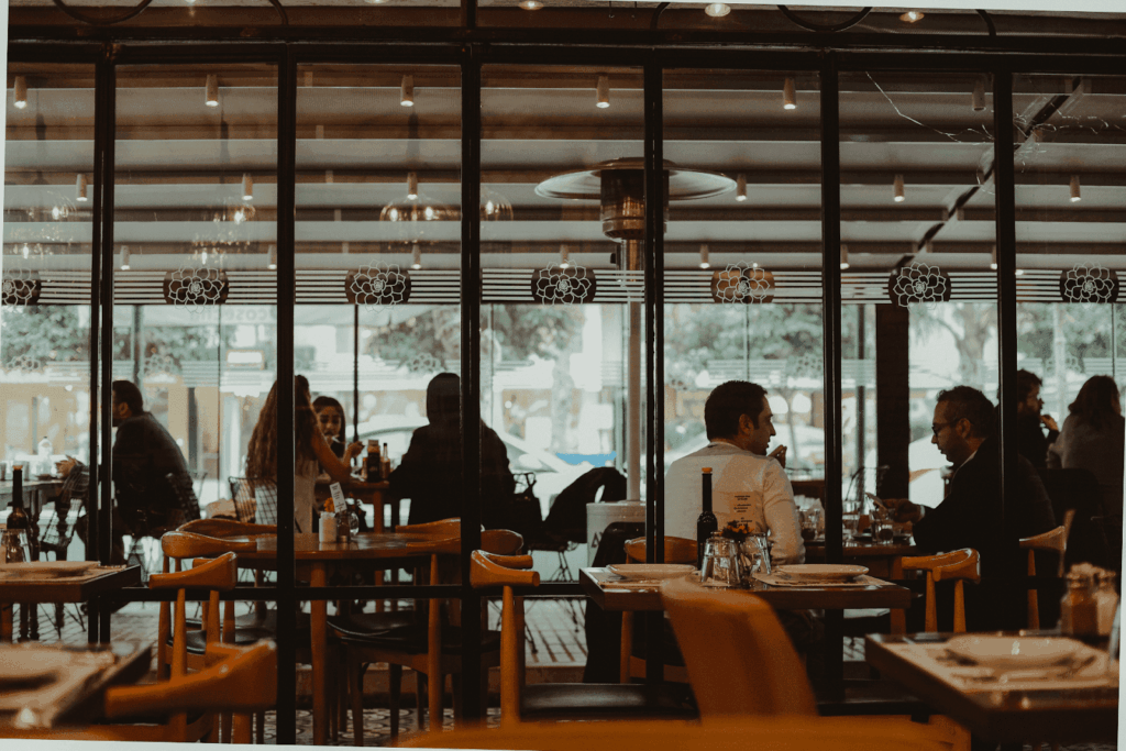 People sitting and talking inside a dimly lit restaurant, viewed through large glass windows.