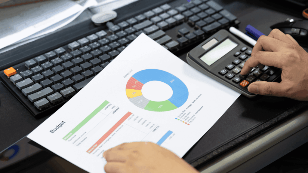 Person using a calculator while looking at a printed budget chart.