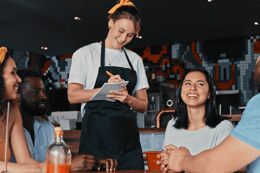 Smiling server taking orders from a group of diners at a restaurant.