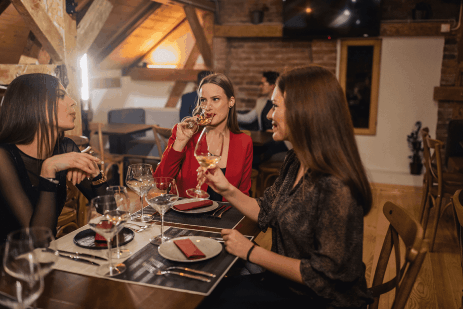 Three women in a restaurant, sipping wine and chatting at a dinner table.