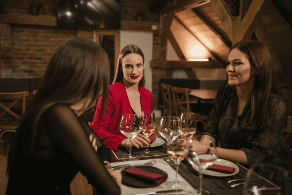 Three women sitting at a restaurant table with wine glasses, talking and smiling. 